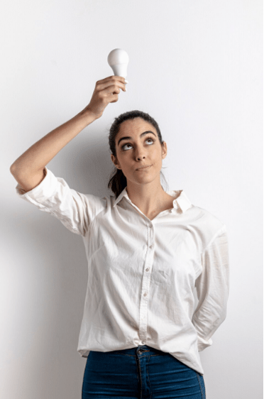 Femme en chemise blanche tenant une ampoule allumée au-dessus de sa tête, symbolisant une idée ou une prise de conscience.