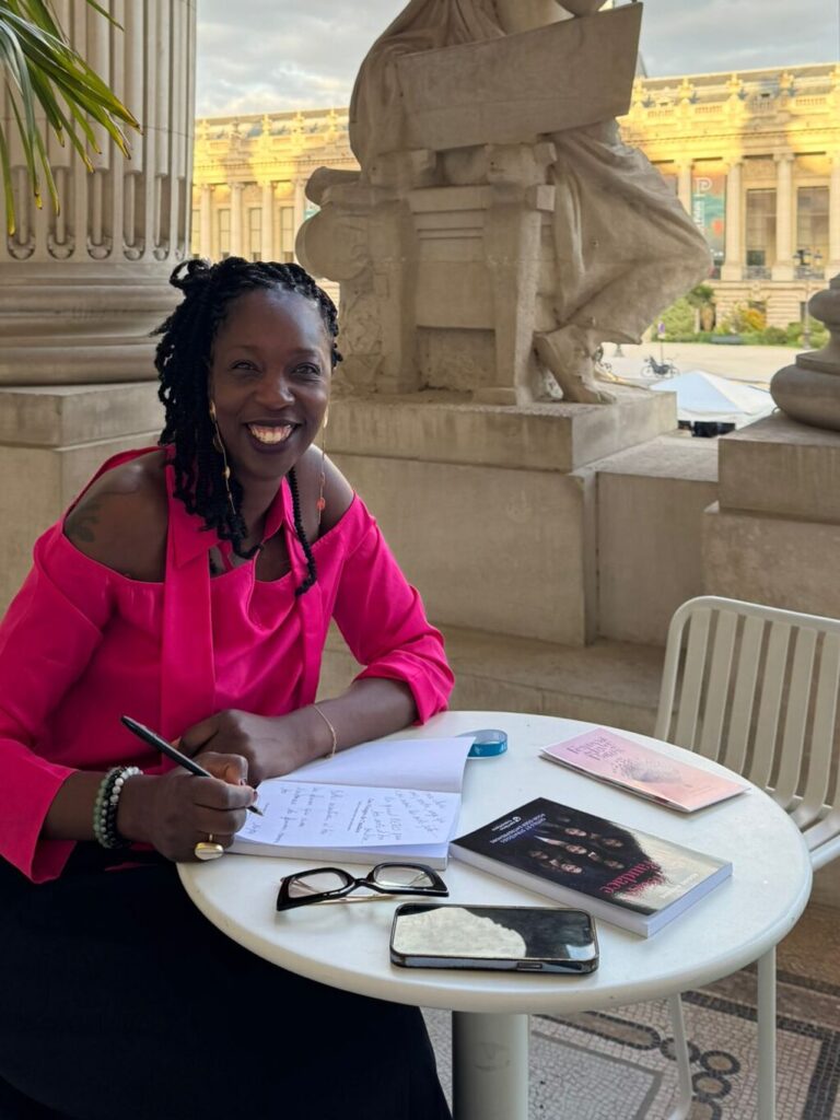 Rosine Bassène souriante, assise à la terrasse d'un café, dédicaçant son livre Les Visages de l'audace.