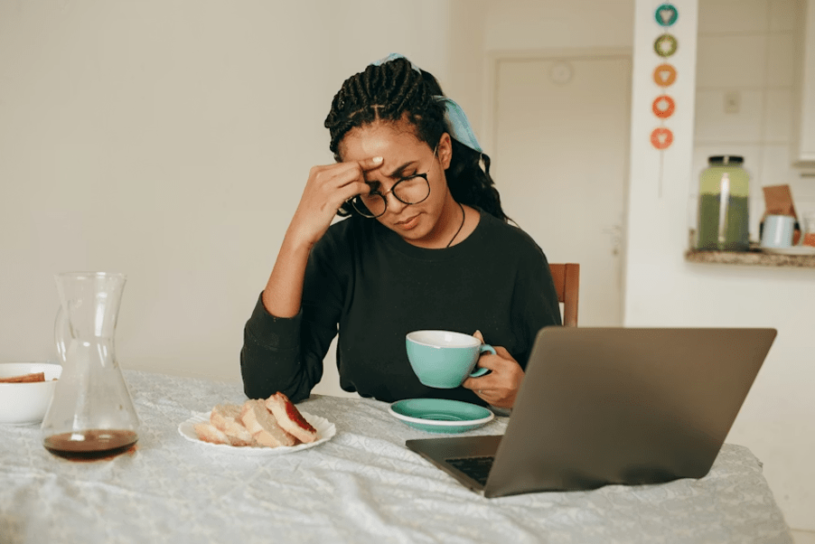 Femme entrepreneure fatiguée se tenant la tête devant son ordinateur avec une tasse de café.