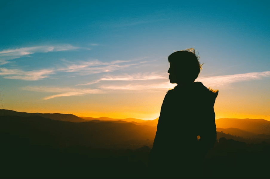 Silhouette d'une personne sereine regardant un coucher de soleil sur les montagnes.